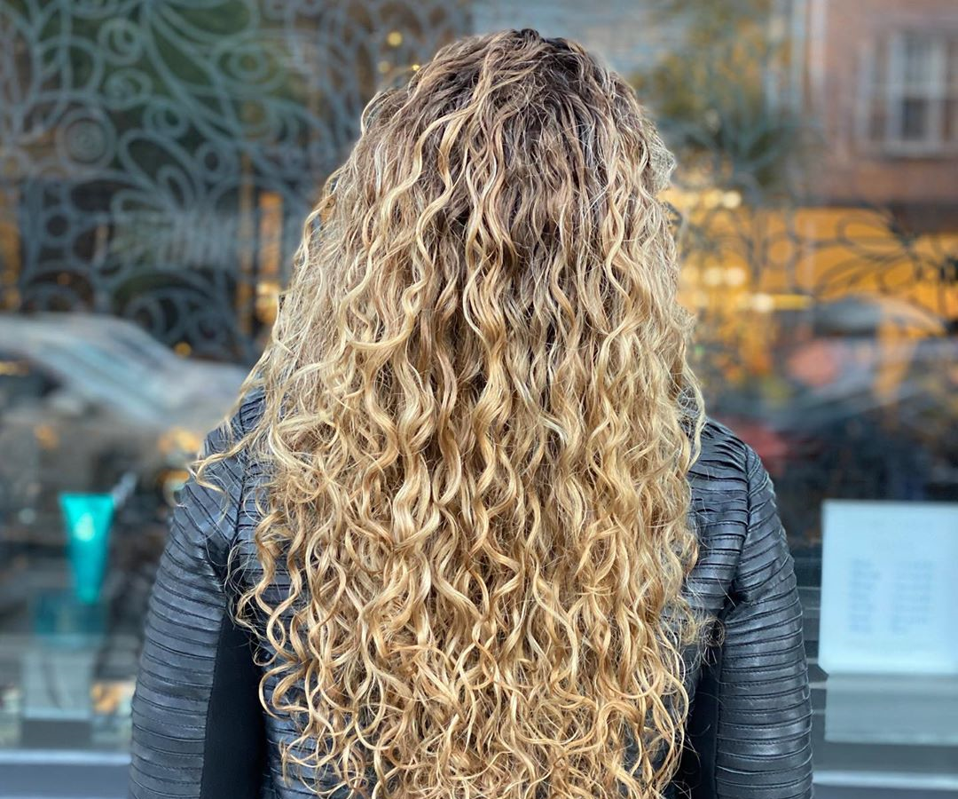woman with long curly balayage facing away towards a stylis store-front